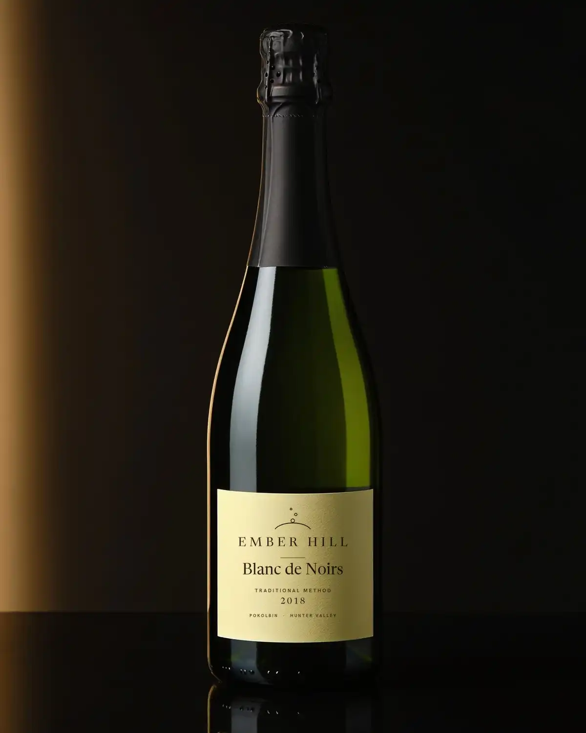 A bottle of Ember Hill Blanc de Noirs with a cream label on a dark table