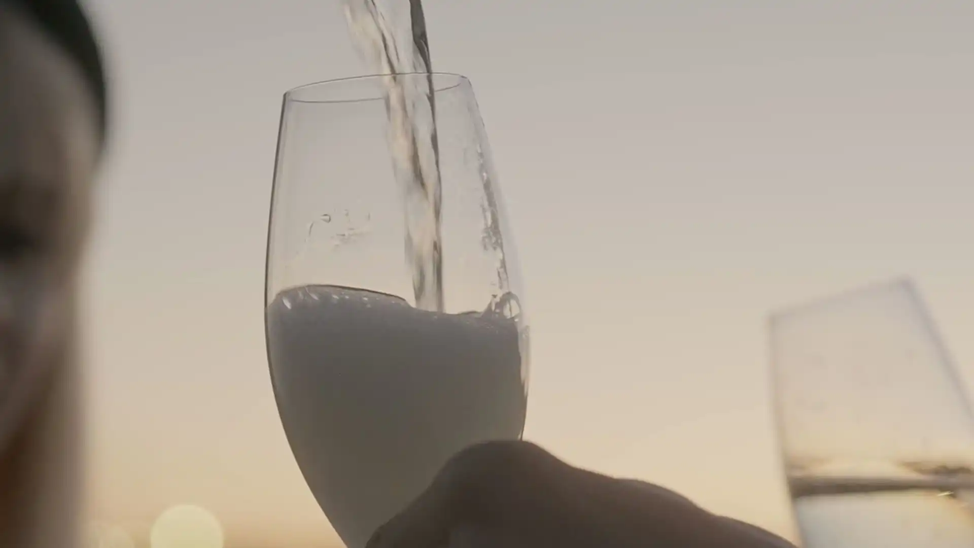 Sparkling wine being poured into a glass held up against a pale dusk sky