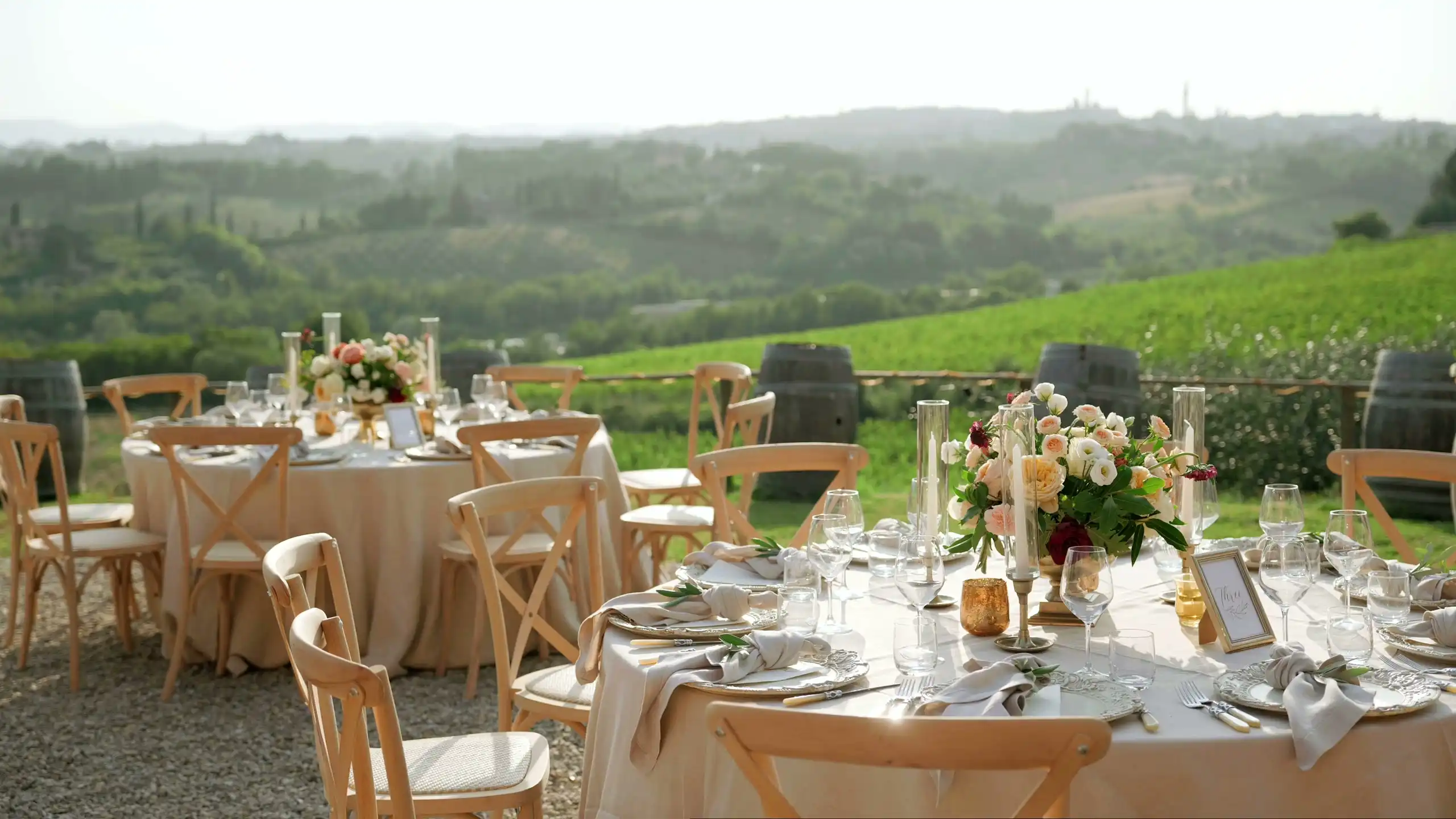 Round tables set with white cloths on a lawn above vineyards