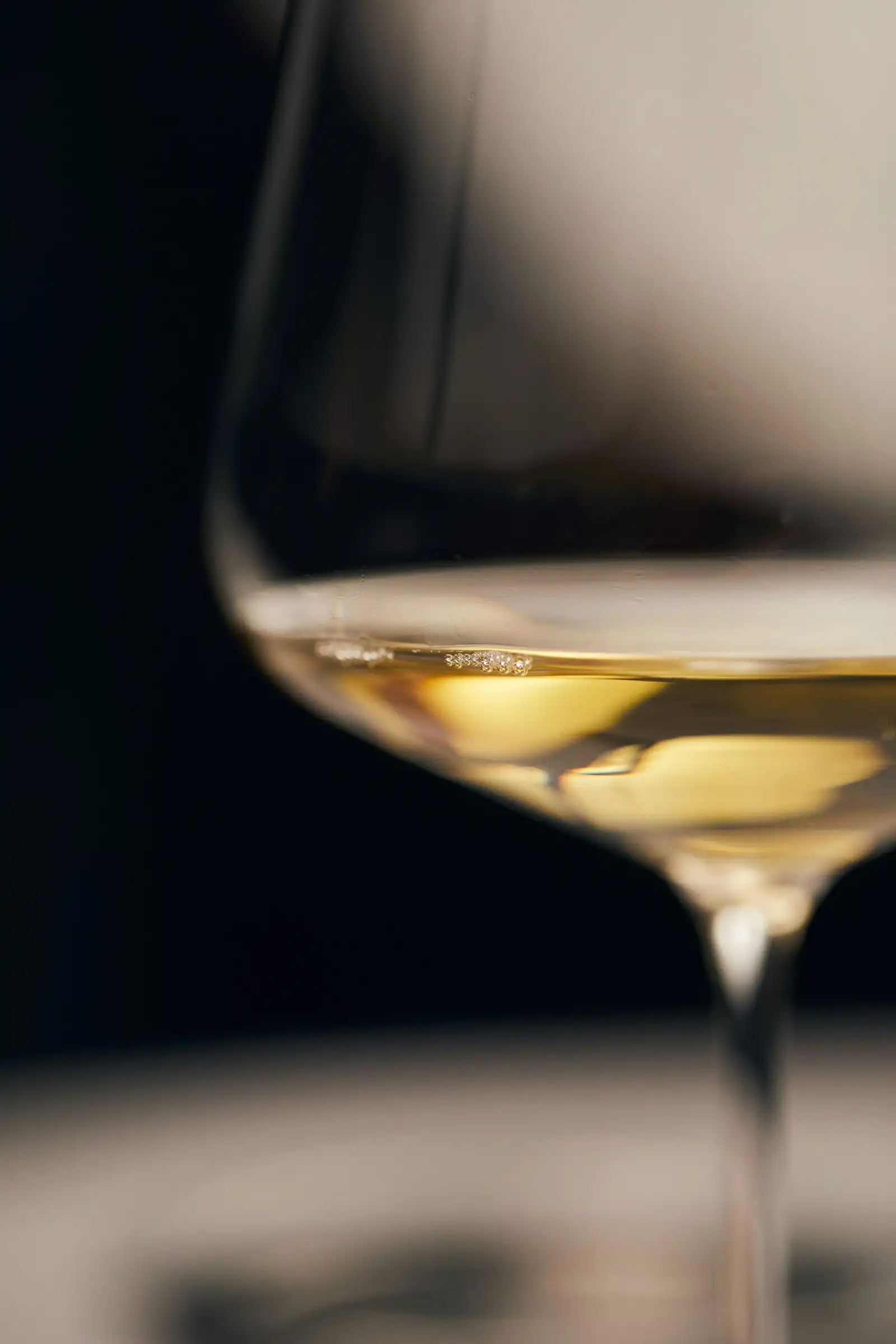 A glass of pale sparkling wine on a dark table, light on the rim