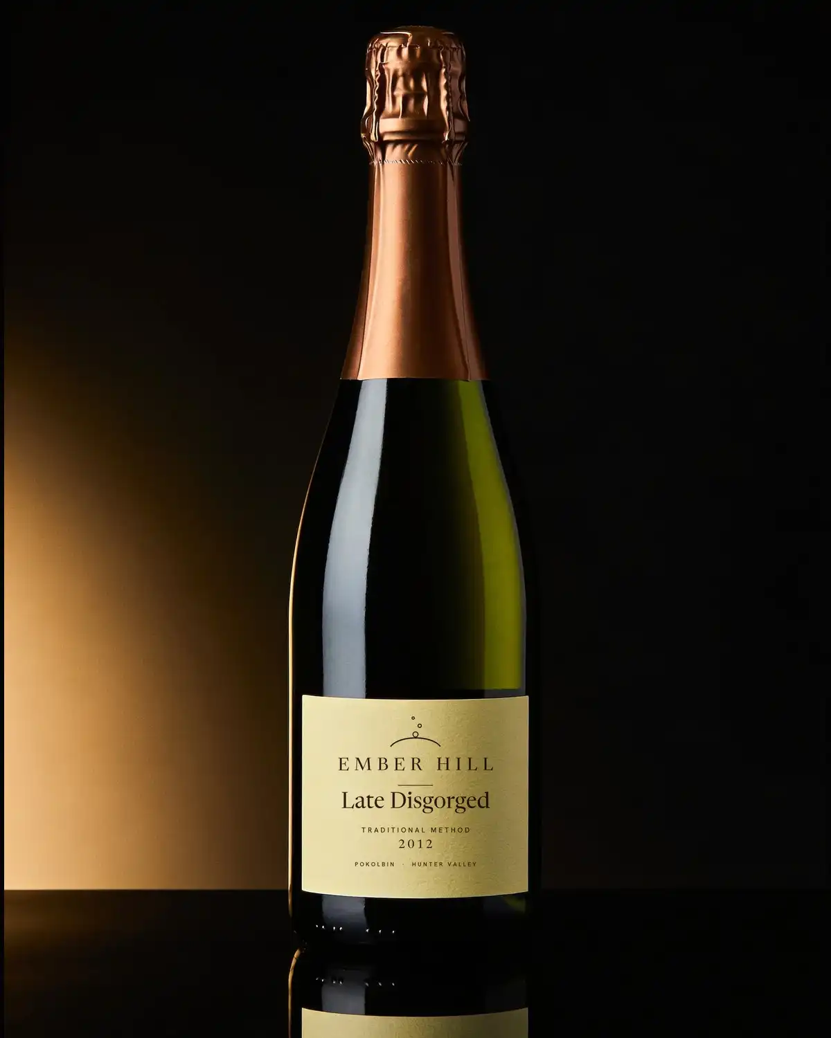 A bottle of Ember Hill Late Disgorged 2012, cream label, on a dark table