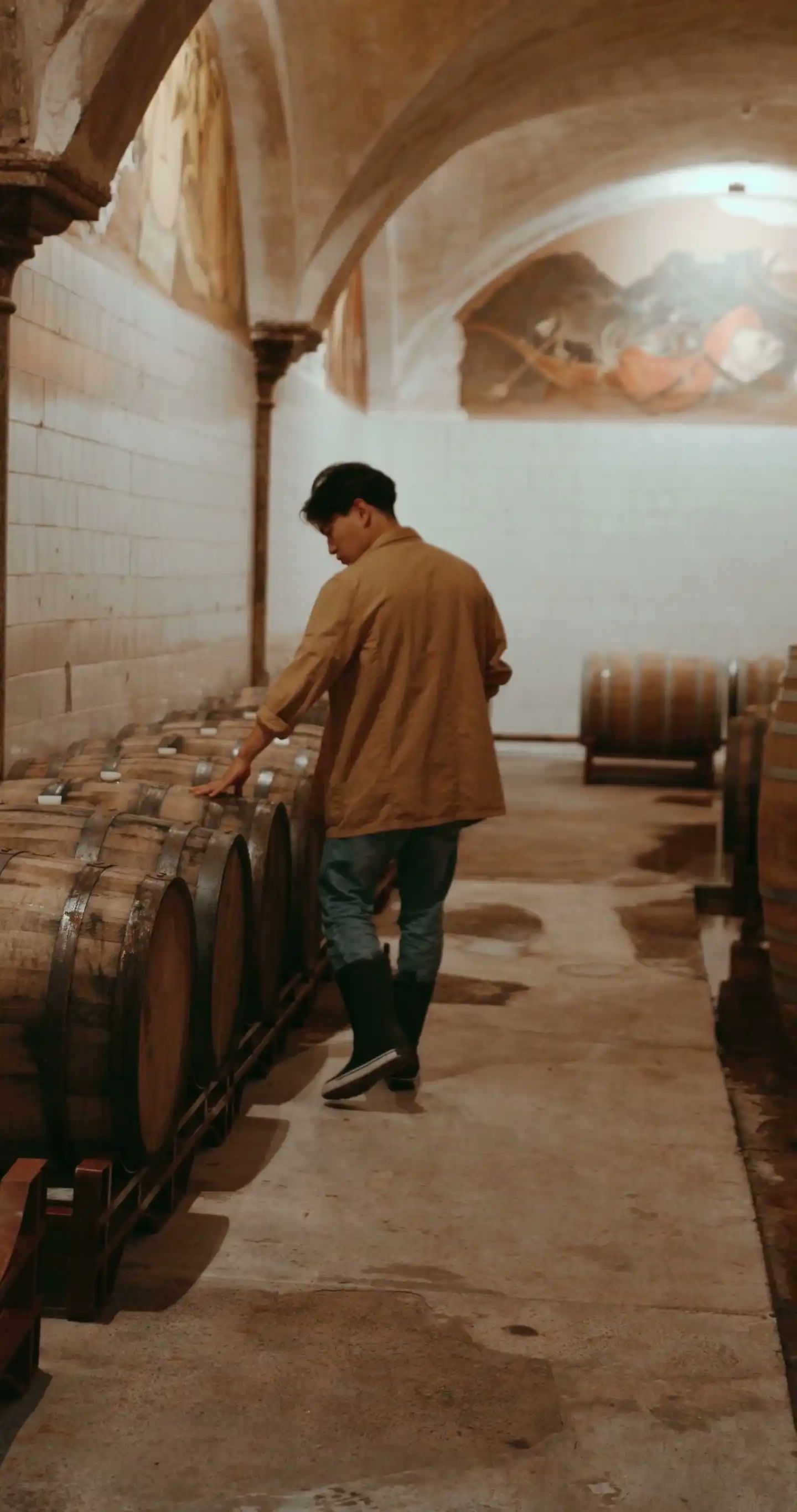 A winemaker walking between rows of barrels in a cellar