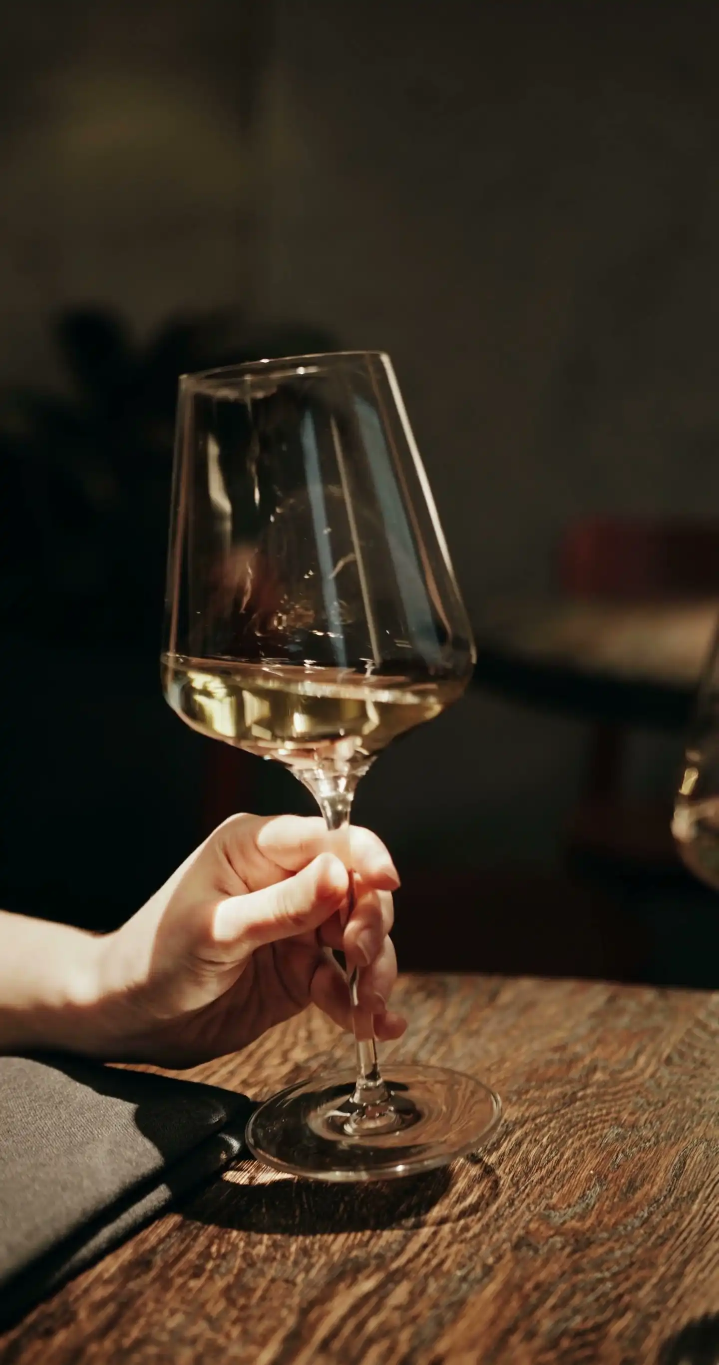 A hand swirling white wine in a glass on a wooden table