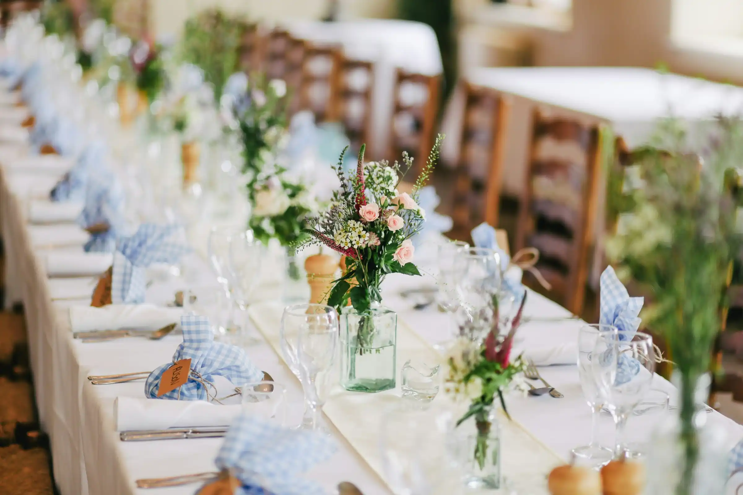 A long table set with white linen, glasses and small vases of flowers