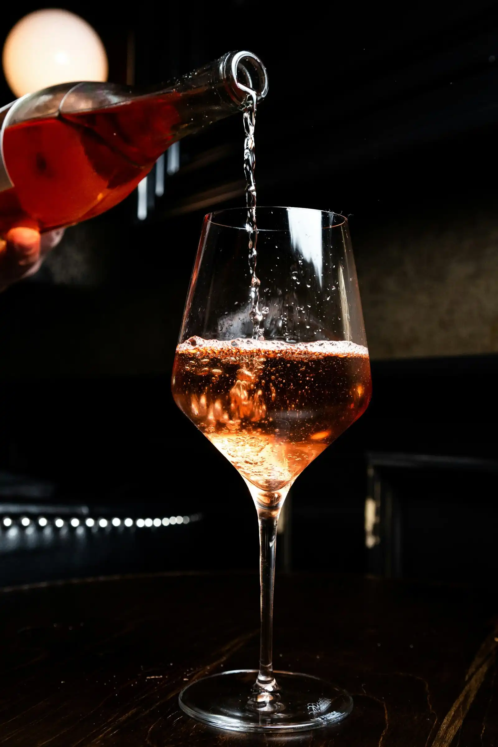 Pale pink sparkling wine being poured into a glass in a dark room
